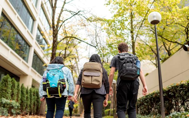 Three students in backpacks walking down the park blocks.