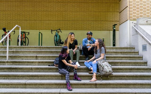Group of four people chatting on steps of library