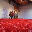 A group of students standing in a field of shredded construction fencing, a sculpture installation in a gallery setting