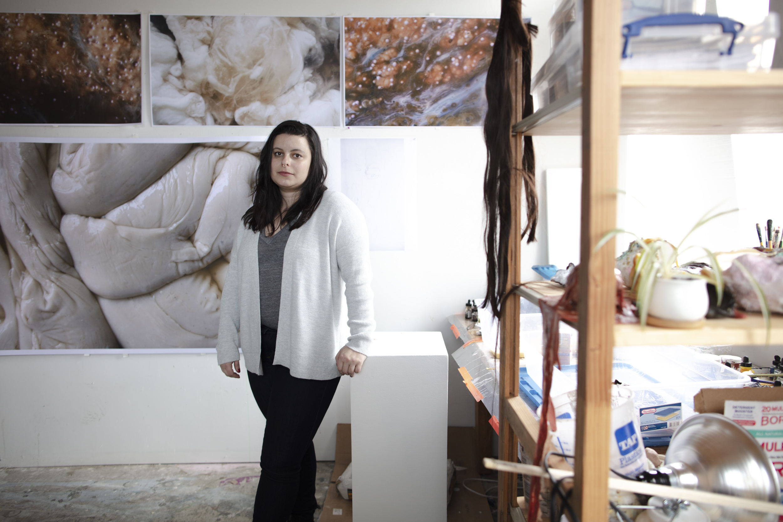 Graduate student Samantha Ollstein standing in her studio surrounded by her artwork
