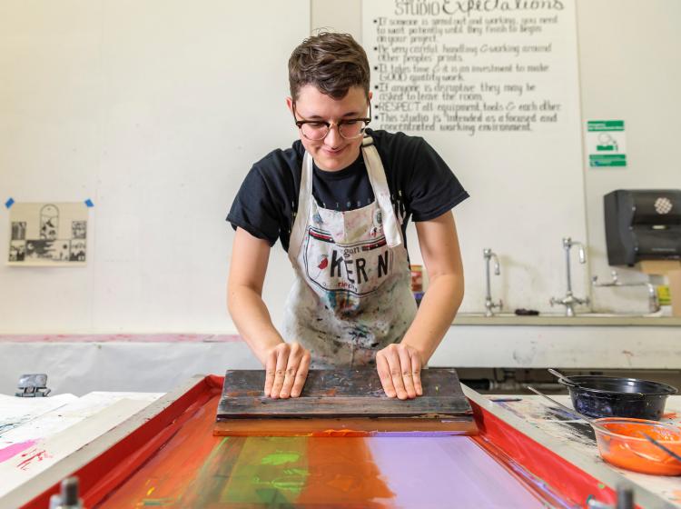Student drawing colorful ink across a silk screen with a squeegee