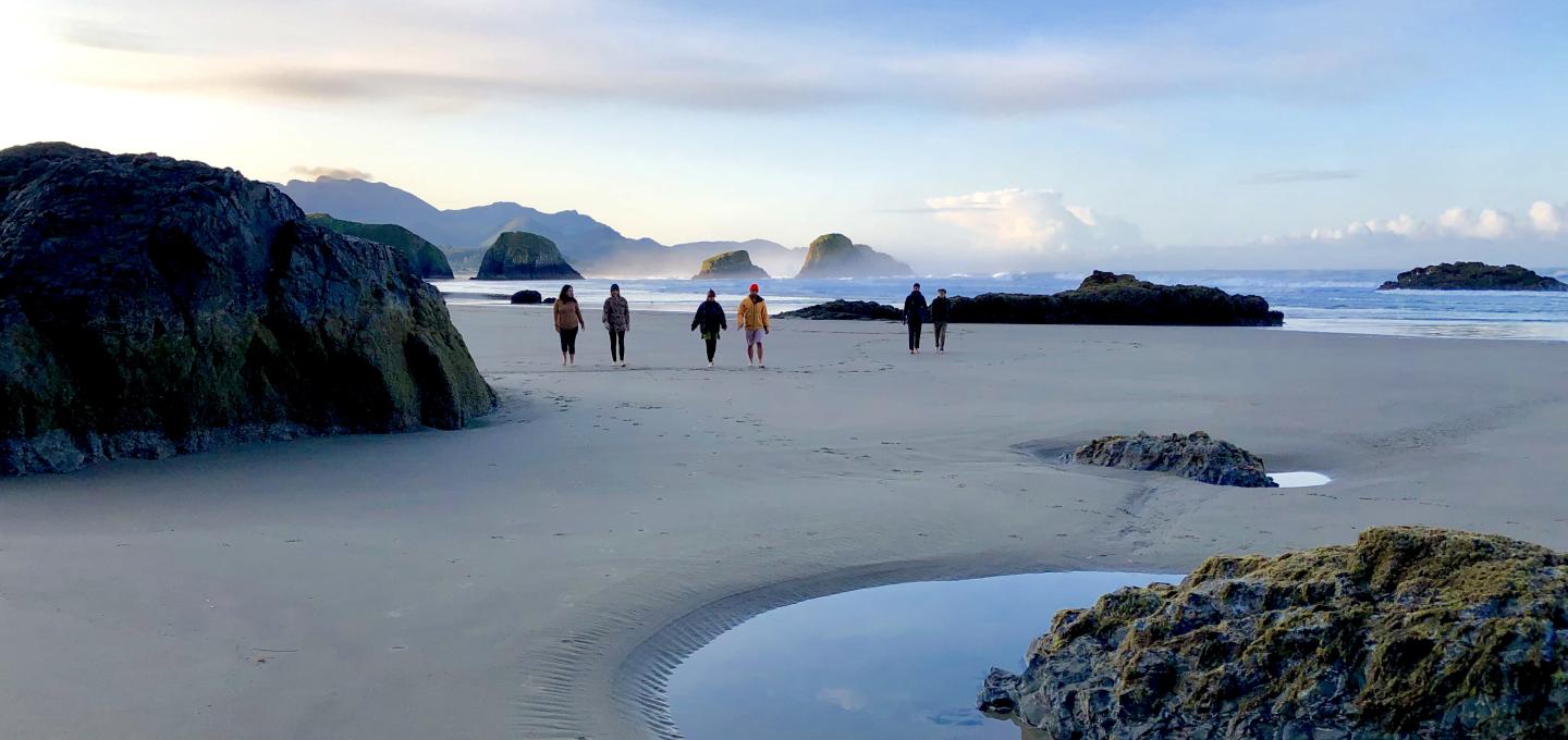 Six students walk along a beach during a field trip to the Oregon Coast.