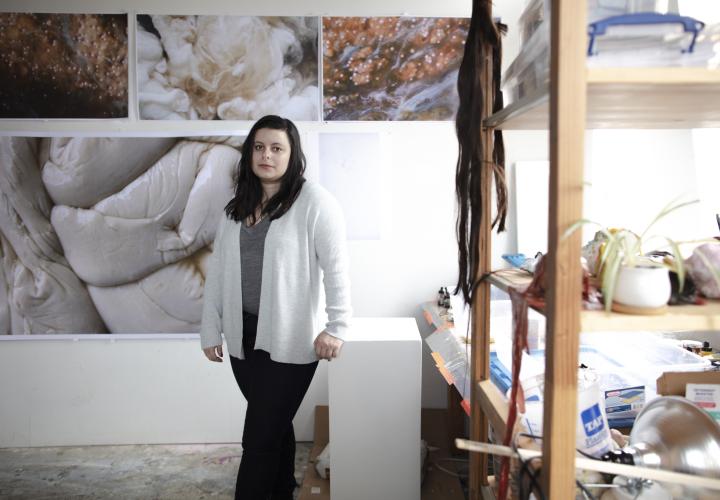 Graduate student Samantha Ollstein standing in her studio surrounded by her artwork
