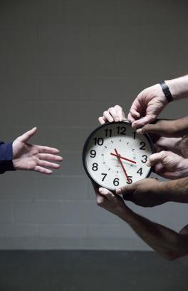 Several sets of hands hold out a clock while a single open hand reaches for it