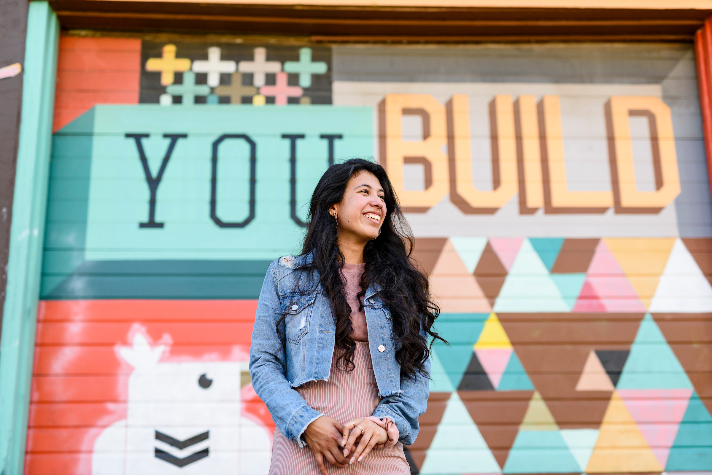 Student standing in front a mural that says "You Build"