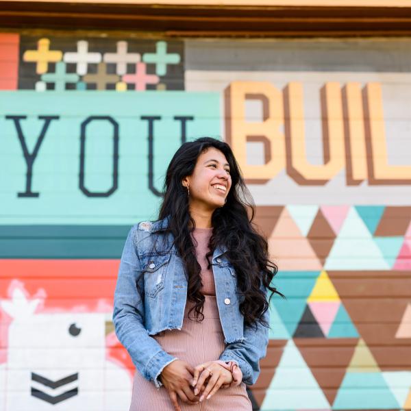 Student standing in front a mural that says "You Build"