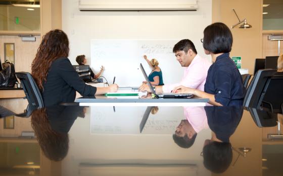 Students in a classroom looking at a whiteboard with tutor. 