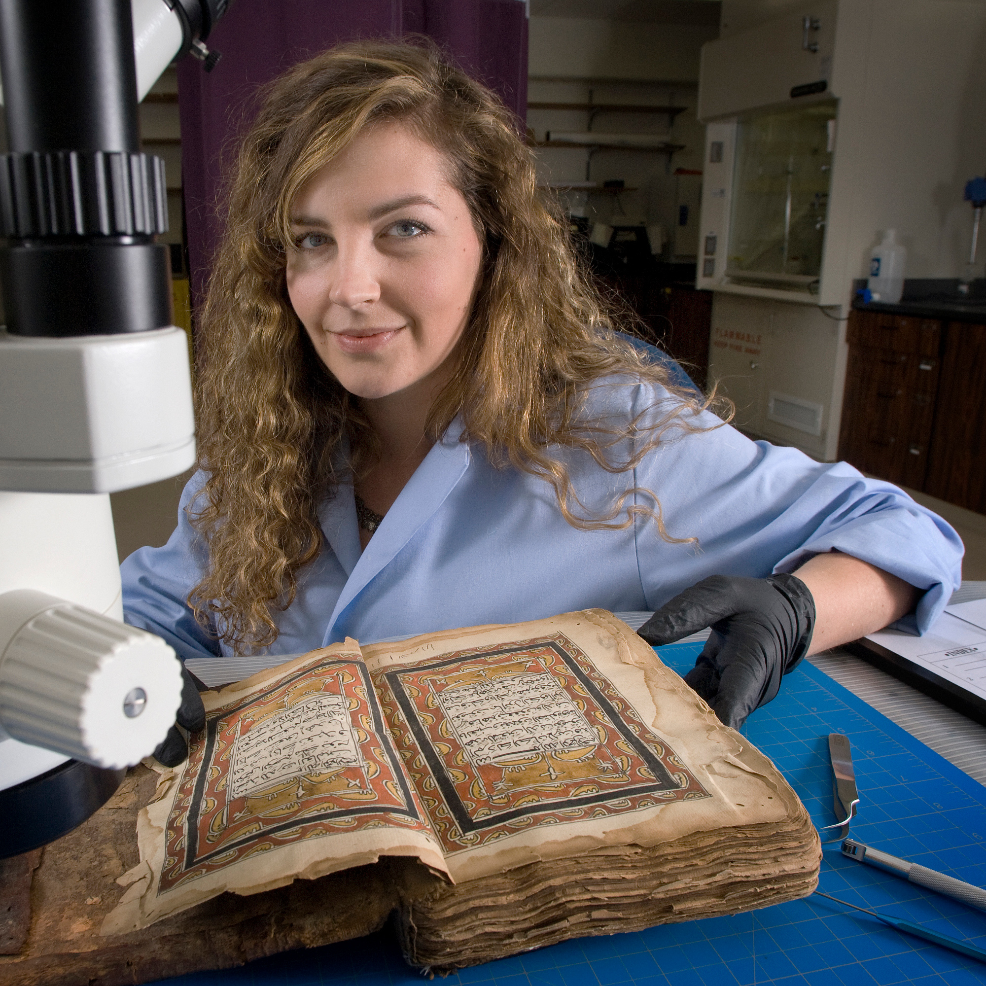 Natasja holding illustrated manuscript with microscope in the foreground