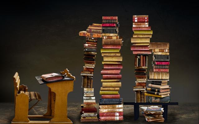 Four tall stacks of books sit in front of an old desk.