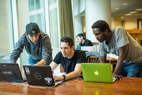 Three male undergraduate students on laptops in library