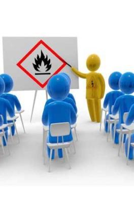 A classroom of people with an instructor pointing to a presention. The presentation is showing a hazard symbol.