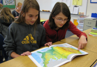 Two student girls looking at C-GEO's student atlas of Oregon