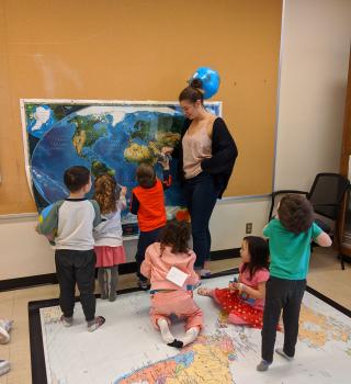 Small children looking at wall map and standing on world map