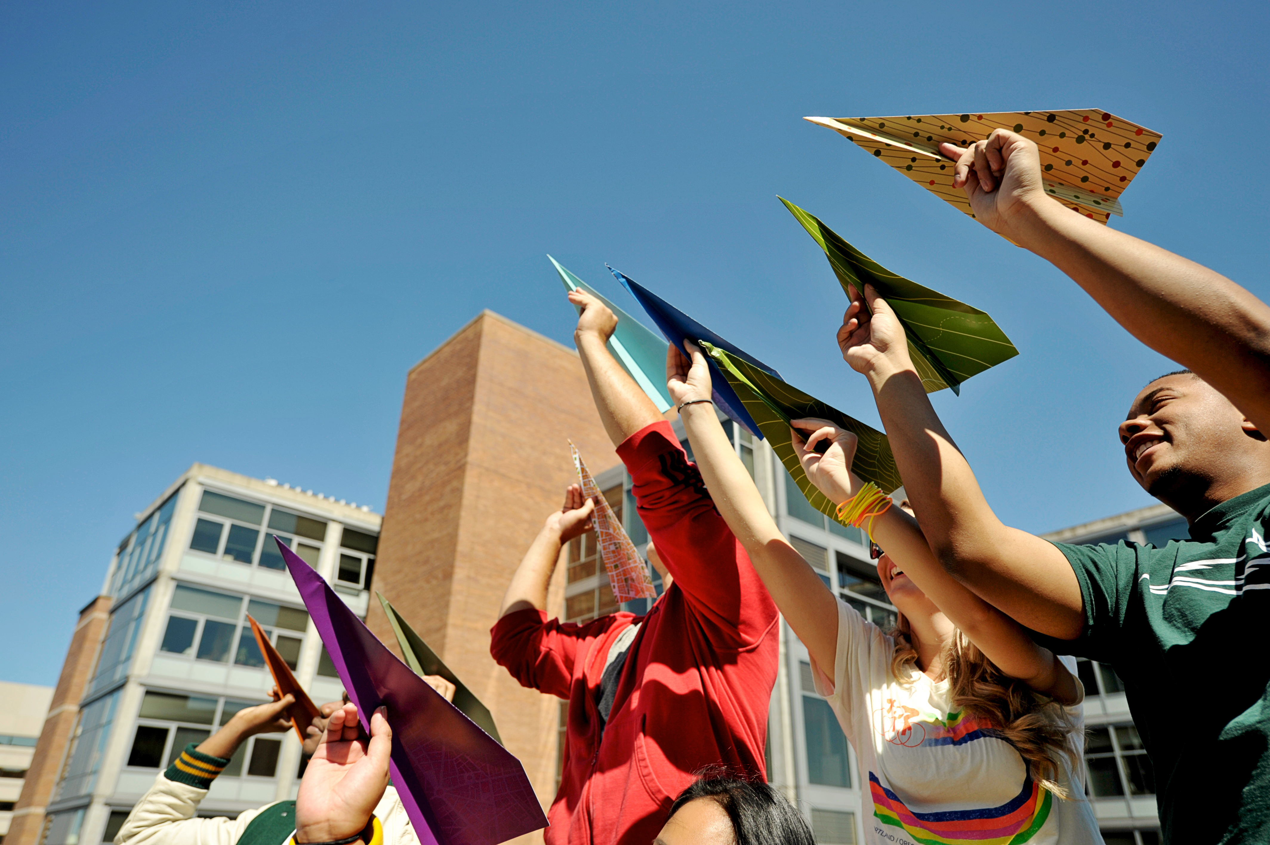 Group of students holding multicolored paper airplanes in the air.