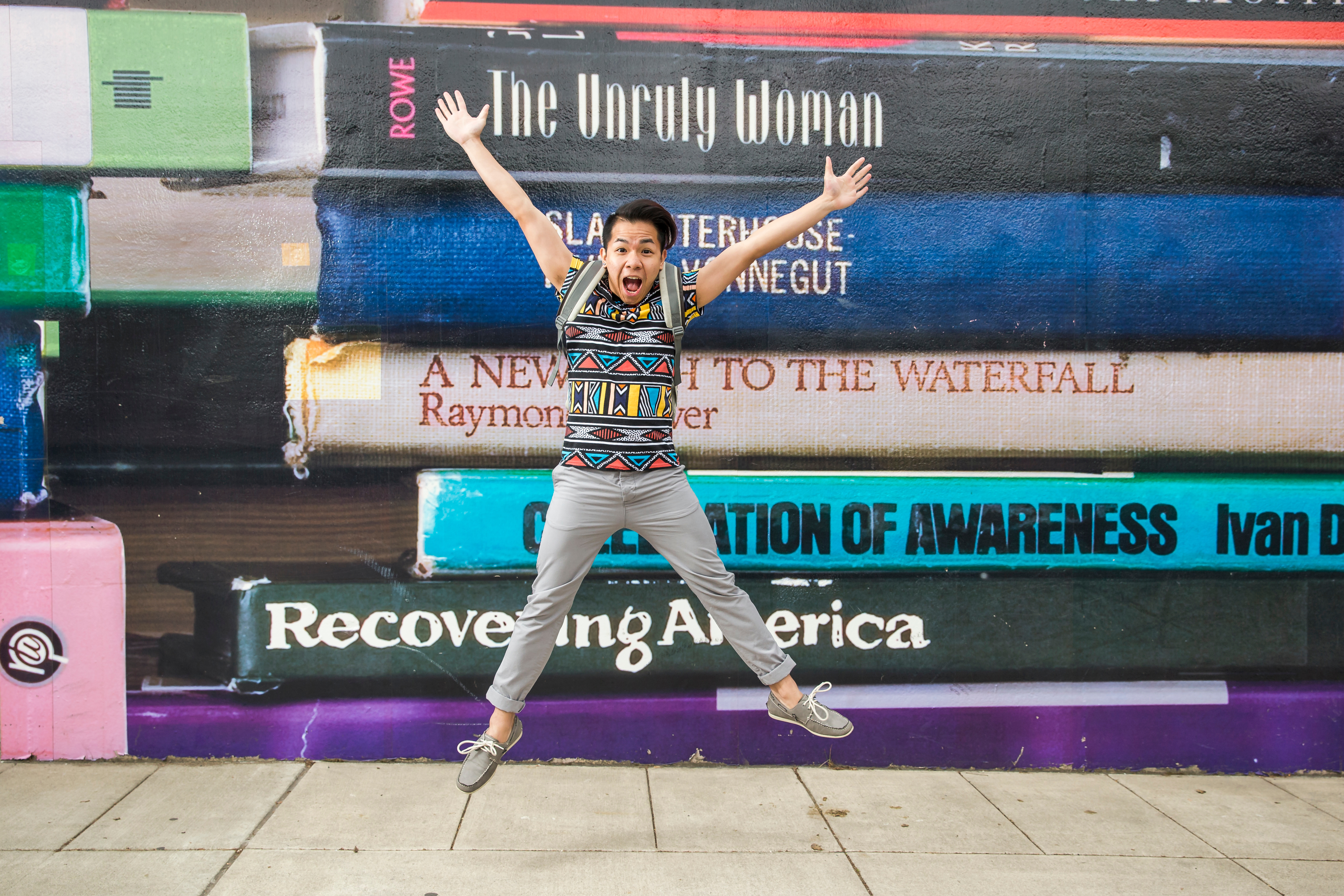 College student jumping in the air in front of an oversized stack of books