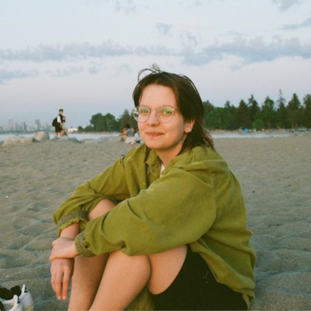 Person with short brown hair wearing a green sweatshirt at the beach.
