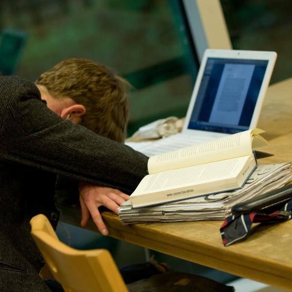 Photo of a student with his head on the desk on front of his laptop resting from study exhaustion