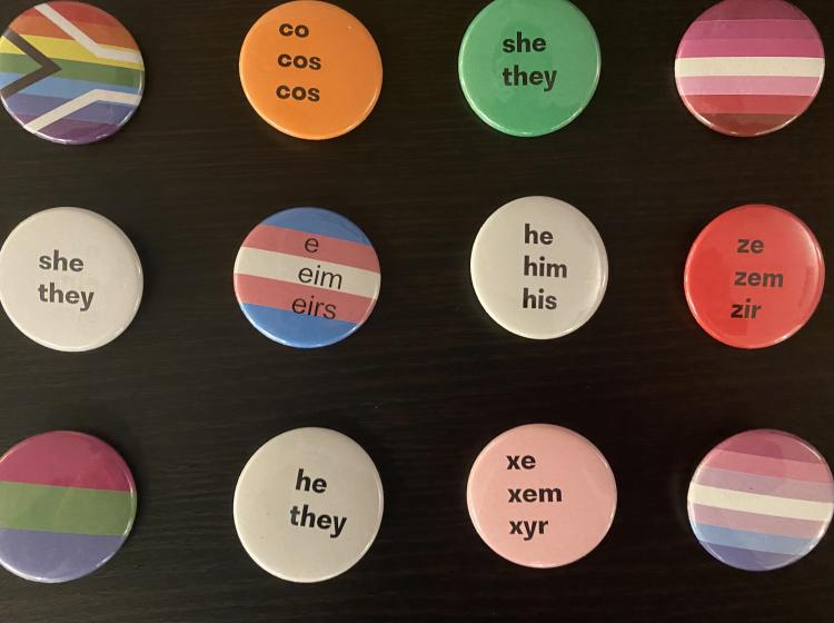Colorful pronoun and identity flag pins are displayed onto of a black backdrop