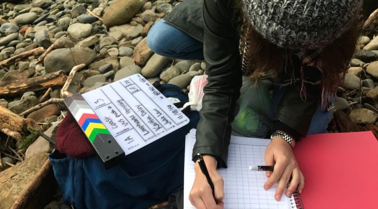 A student writing in a notebook at a rocky beach