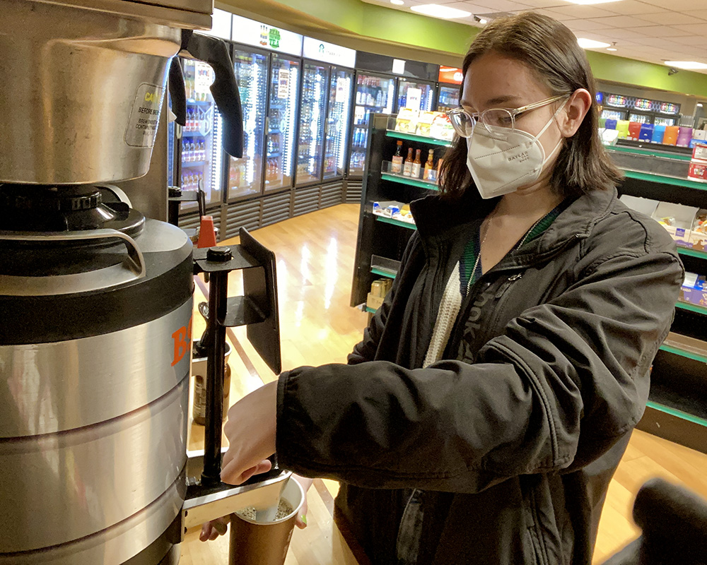 A student fills a cup from the urns of fresh Boyd's coffee in the University Market.