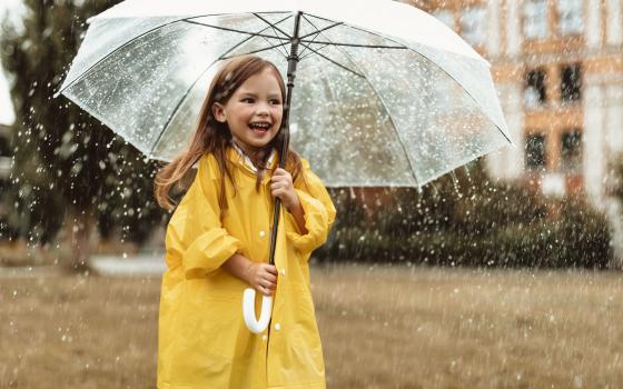 A little girl outside with a rain jacket and umbrella, smiling.