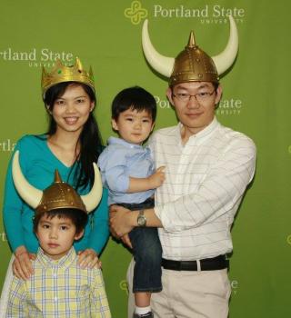 A family of four in front of a PSU backdrop with play viking helmets on.