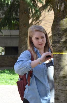 student holds a measuring tape around a tree trunk