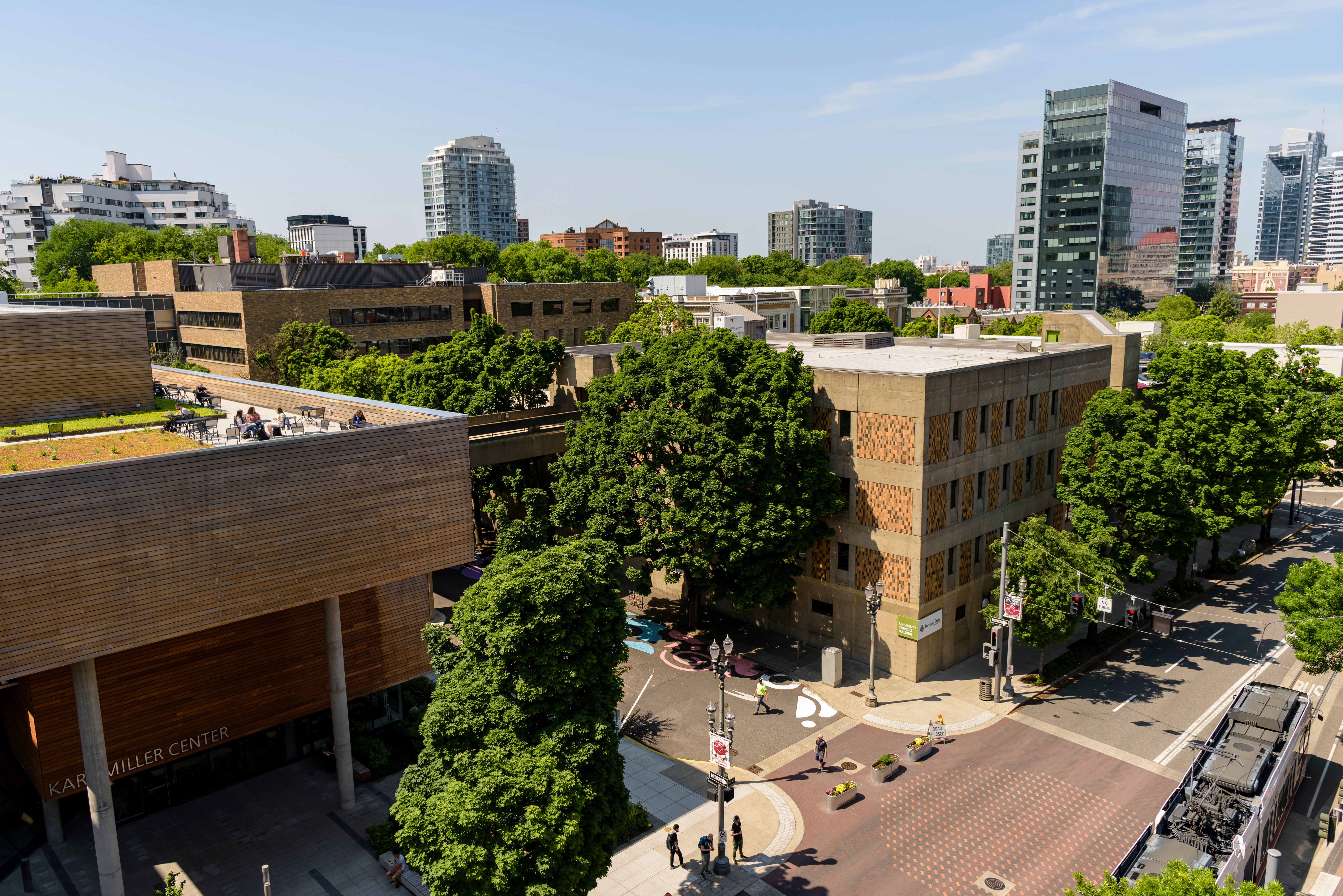 The Karl Miller Center as well as the University Services Building are seen from a drone view on a sunny, morning day. The trees surrounding the building are full and green with leaves.
