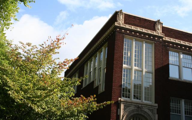 A view of Shattuck Hall looking at the top corner of the building with a single tree on the left, leaves beginning to turn red.