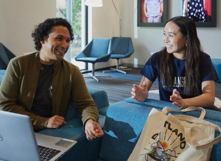 man and woman smiling while talking and looking at a computer