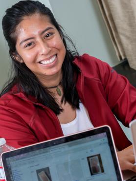 Student in a red sweater smiling with laptop in foreground