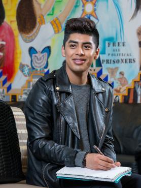 Student in black jacket writing in notebook in from of mural