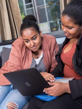 Two students on a coach looking at a laptop