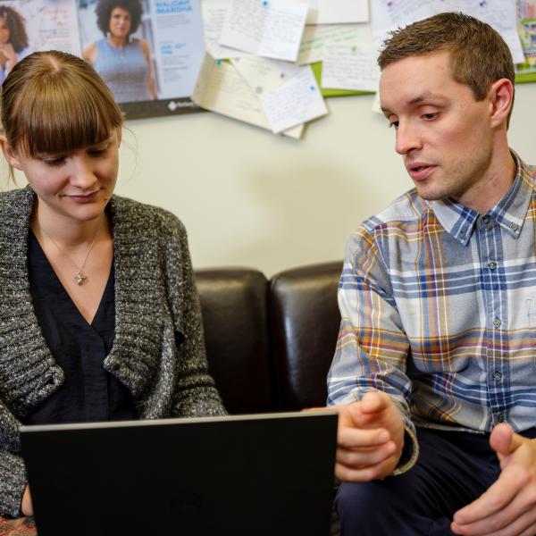 Man with sandy hair and student with sandy hair and bangs look at a laptop together