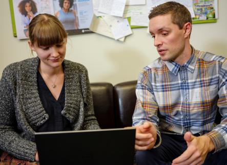 Man with sandy hair and student with sandy hair and bangs look at a laptop together