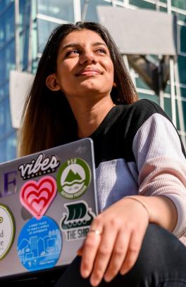 Student with long dark hair sitting with laptop in PSU Urban Plaza