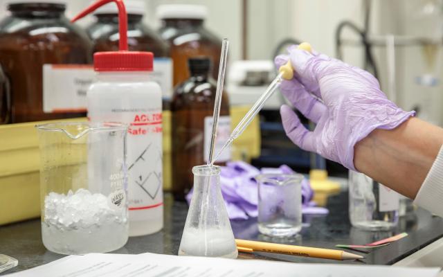 Hand holding a dropper in a chemistry lab