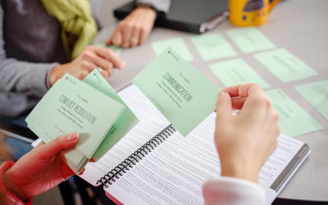 A hand holds a card that says "Communication" in one hand and a stack of index cards in the other.
