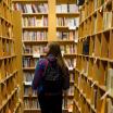 Student with long, sandy hair walks in the aisle of a bookstore