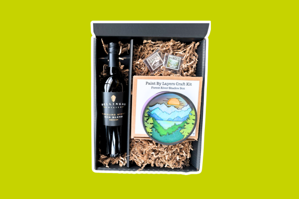Gift box with a bottle of Bellingar Estates wine, two chocolates and a paint layers craft kit of a mountain scene with trees and the sun.