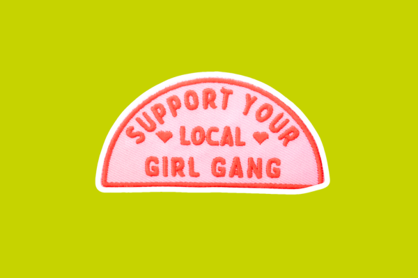 A pink patch that says in dark pink letters "Support your local girl gang".