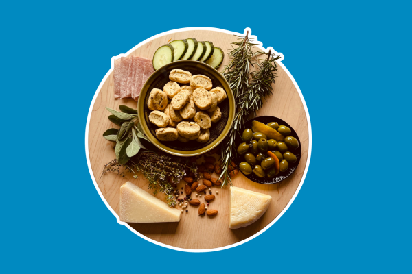 Charcutier board with olives, cheese, cucumbers, sprigs of rosemary and other garnishes surrounding a bowl of friselles.