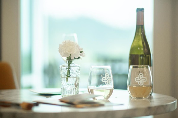 A bottle of wine on a table with two PSU branded glasses and a white flower in a glass of water.