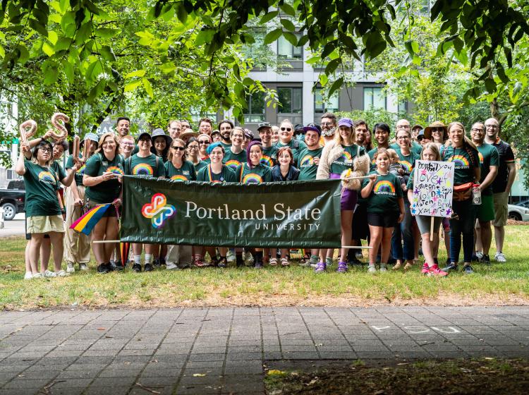 Group photo of students, alumni and staff posing in front of a Portland State University banner in the North Park Blocks before the Pride Parade.