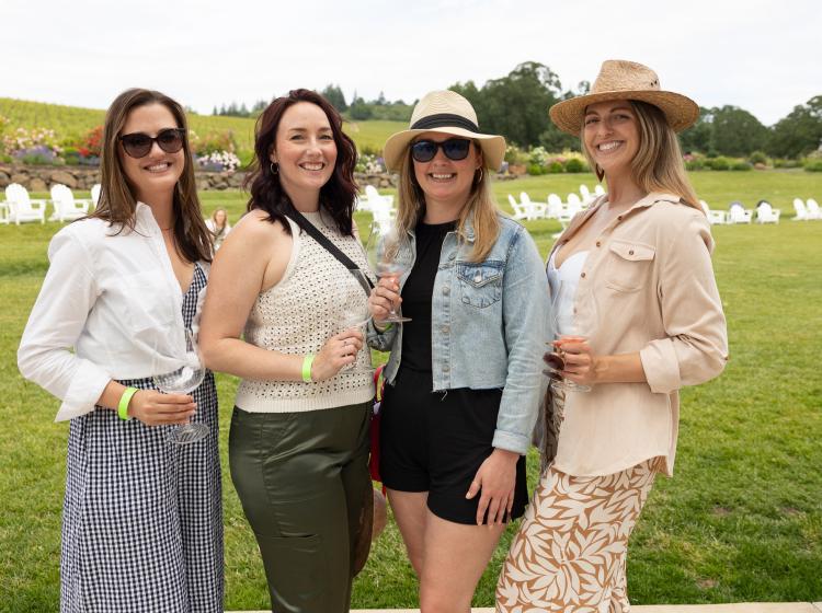Four women posing with their wine glasses outside in the vineyard of Stoller Family Estate