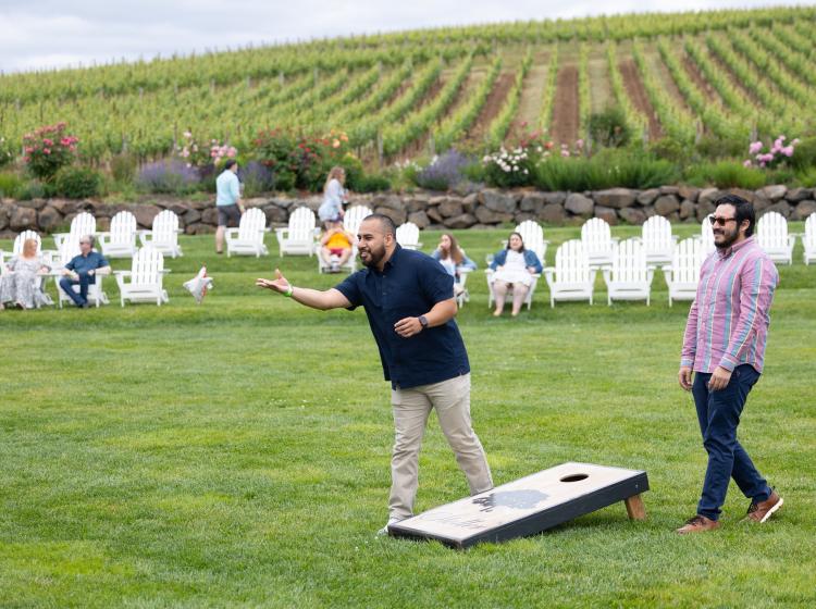 Two attendees playing cornhole outside at Stoller with the vineyard in the background.