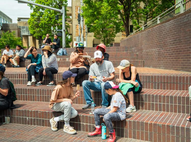 A family sitting on the steps at the Urban Plaza eating paletas after volunteering at Serve the City Day 2025.
