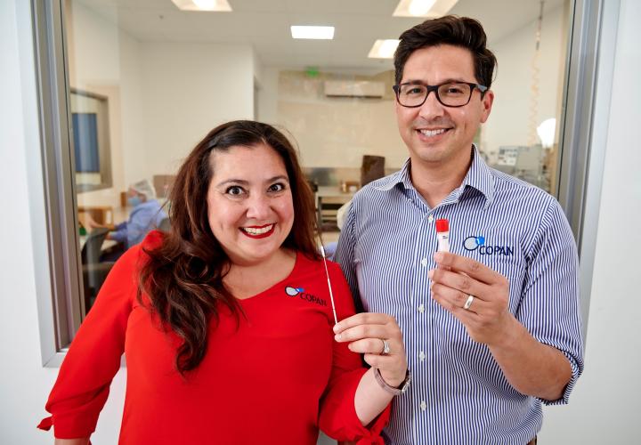 Gabriela and Franco holding up a COVID-19 testing swab kit