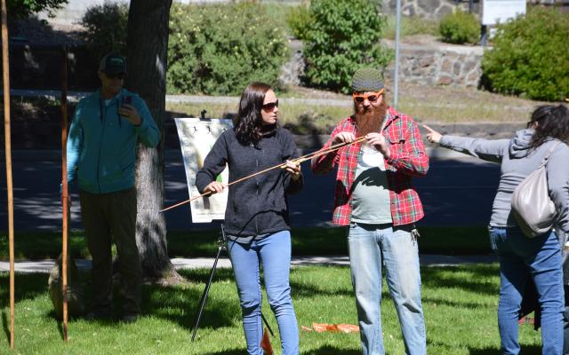 Bend Oregon Archaeology Roadshow volunteer explains how to use the atlatl spear thrower to a visitor at the 2019 event; photo by Beverly Clement