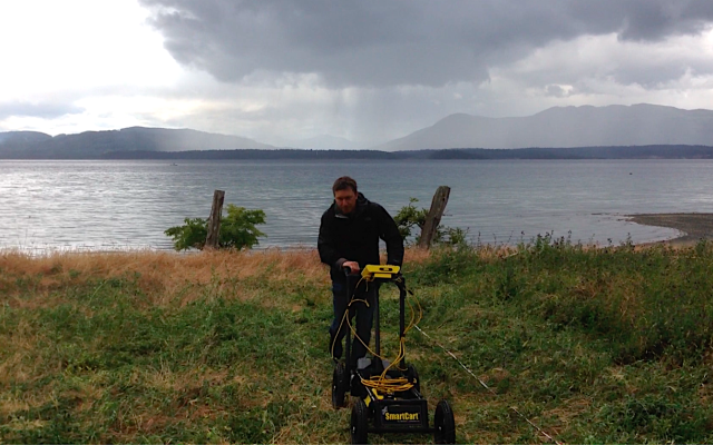 Man using ground penetrating radar on grassy field